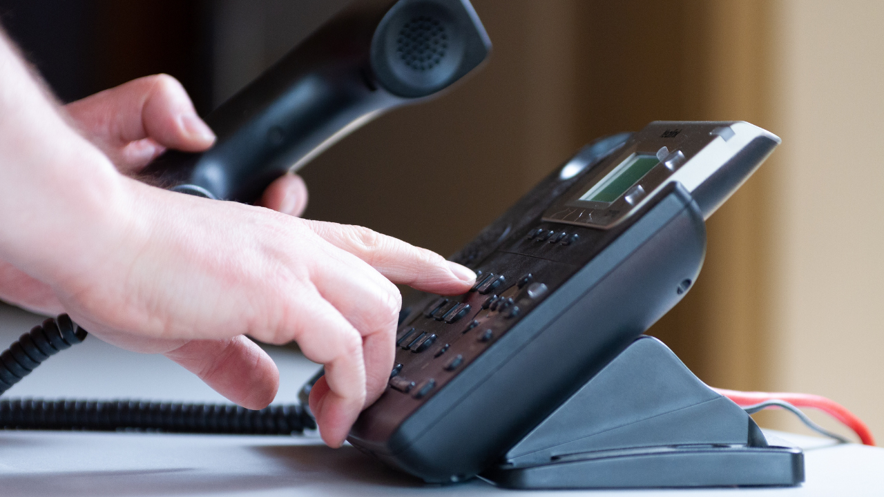 A hand holds an office phone while dialling a number
